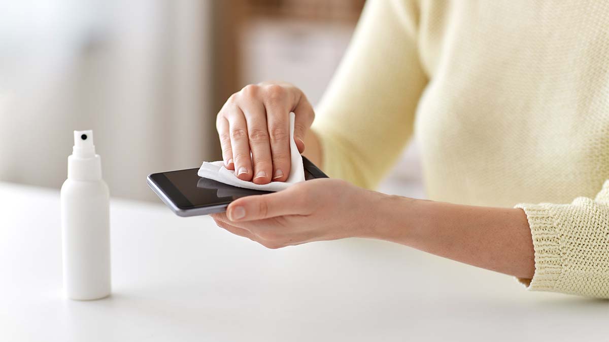 Close up of woman hands cleaning smartphone with hand sanitizer and tissue